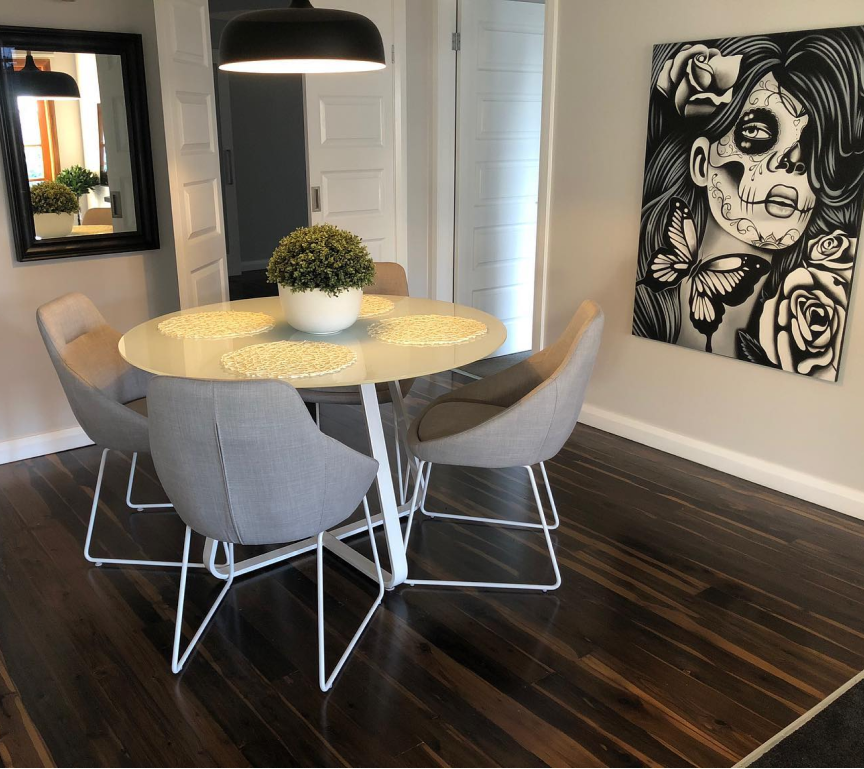 Small room with 2 chairs and a circular table on a newly polished floor with a skull painting on the wall