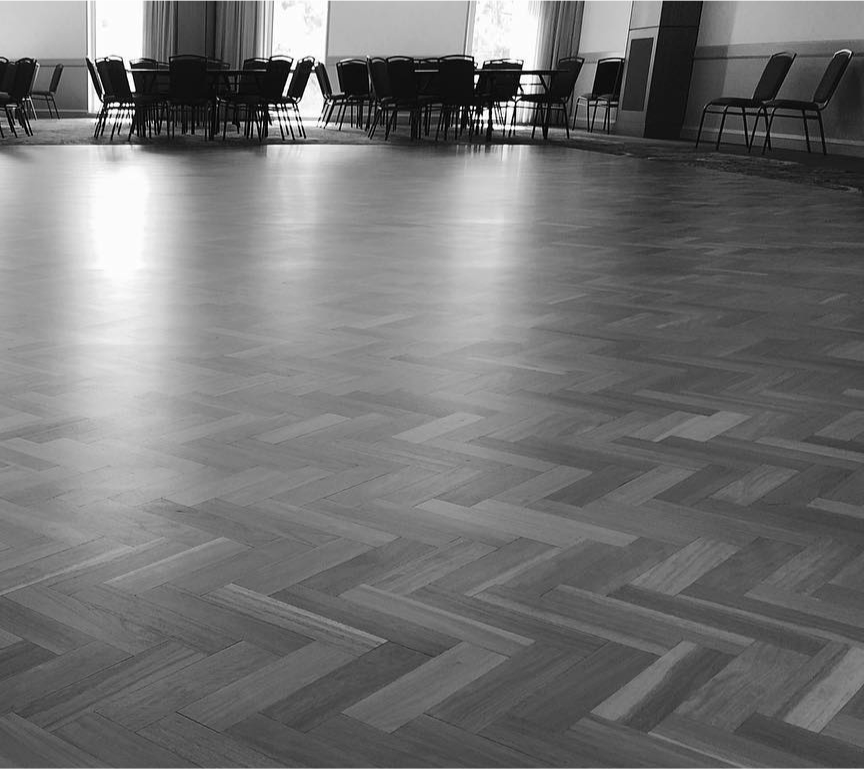 Black and White photo of a wooden floor in crossed patterns with chairs viewed a far